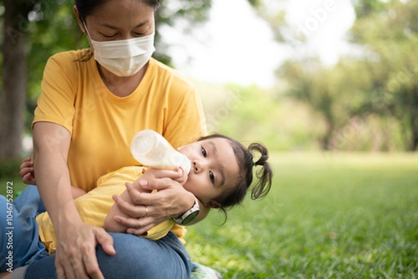 Obraz Asian daughter drinking milk in a bottle Sleep happily on mom's lap in the park on the weekend