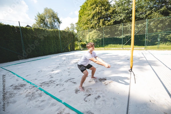 Fototapeta Young man in a ready position, preparing to receive or dig a volleyball on a sandy court. Capturing the intensity and focus of beach volleyball in an outdoor setting