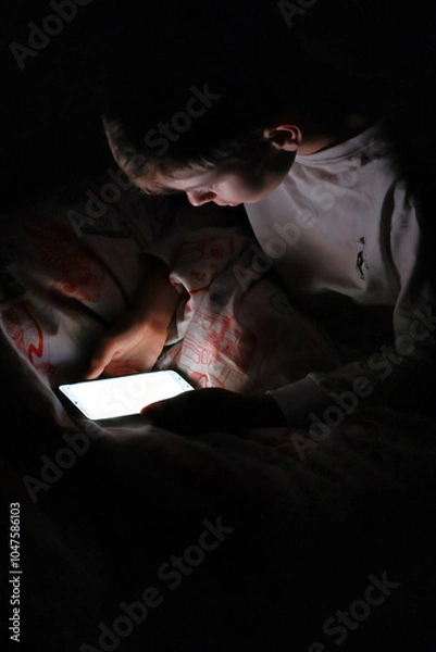 Obraz Kid sitting in bed at night with his smartphone on