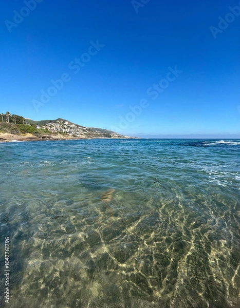 Obraz A breathtaking view of crystal-clear ocean water at Laguna Beach, with gently rolling waves and a cloudless blue sky. The sandy seafloor is visible through the transparent water.