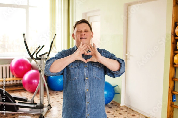 Obraz A man with Down syndrome is making a heart shape with his hands in a gymnasium.
