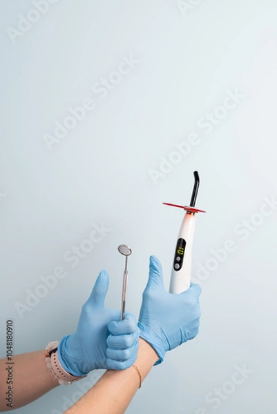 Fototapeta Dental professional holds curing light and mirror tools in a bright clinic setting during an appointment