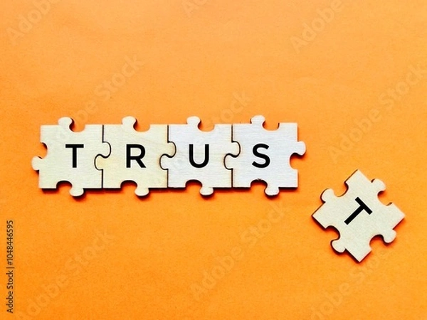 Fototapeta Concept image of broken trust made on wooden puzzle with detached alphabet shot on orange background. Emotion, business, finance, relationship concept design.