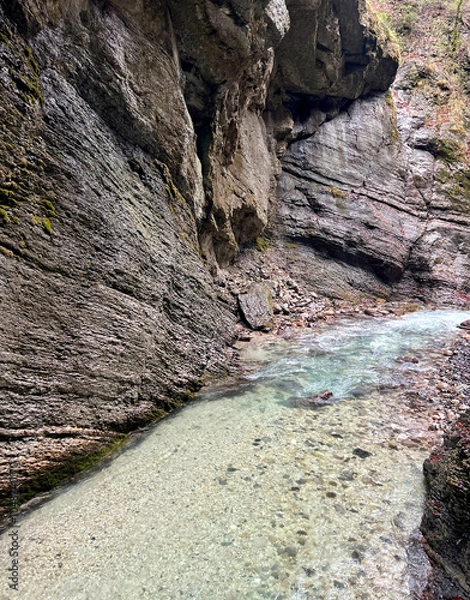Fototapeta The beautiful stream flows through the rocky valley of Partnachklamm Gorge, where lush moss clings to stones, creating a vibrant and serene natural scene in Garmisch-Partenkirchen.