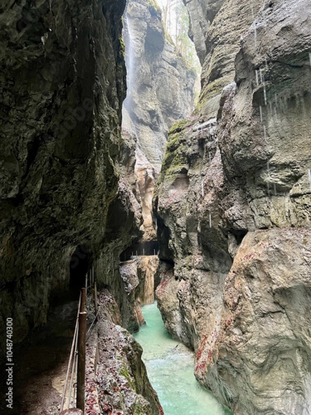 Fototapeta The beautiful stream flows through the rocky valley of Partnachklamm Gorge, where lush moss clings to stones, creating a vibrant and serene natural scene in Garmisch-Partenkirchen.