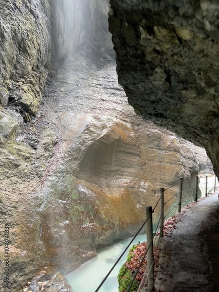 Fototapeta A narrow walkway winds through the rock cliffs at the valley's base alongside a flowing stream at Partnachklamm Gorge, Garmisch-Partenkirchen, offering a stunning alpine experience.