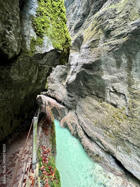 Fototapeta A narrow walkway winds through the rock cliffs at the valley's base alongside a flowing stream at Partnachklamm Gorge, Garmisch-Partenkirchen, offering a stunning alpine experience.