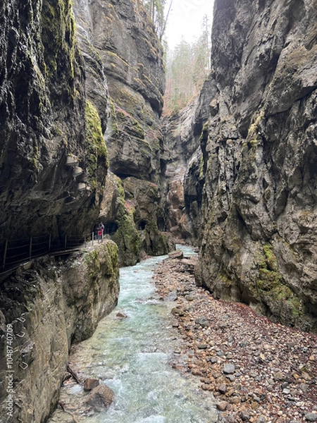 Fototapeta The beautiful stream flows through the rocky valley of Partnachklamm Gorge, where lush moss clings to stones, creating a vibrant and serene natural scene in Garmisch-Partenkirchen.