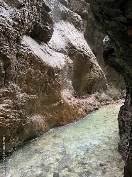 Fototapeta The beautiful stream flows through the rocky valley of Partnachklamm Gorge, where lush moss clings to stones, creating a vibrant and serene natural scene in Garmisch-Partenkirchen.