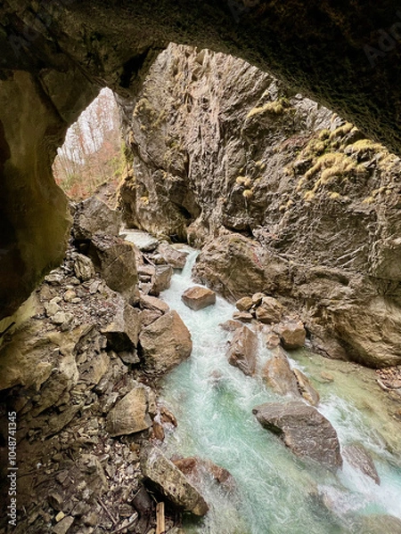Fototapeta A powerful stream flows through the rocky riverbed of Partnachklamm Gorge, winding between towering cliffs and creating a dramatic, rugged valley scene in the Bavarian Alps.