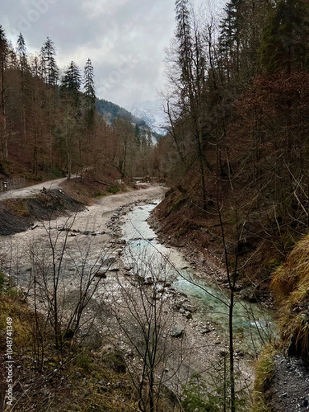 Fototapeta A stream flows from the valley of Partnachklamm Gorge into a lush forest with the majestic mountain range as a backdrop, creating a serene, natural scene in Garmisch-Partenkirchen.