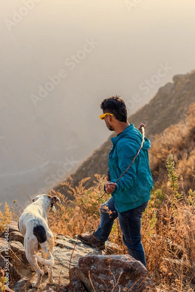 Fototapeta hombre joven parado a orillas de una montaña mirando al frente acompañando e su perro 
