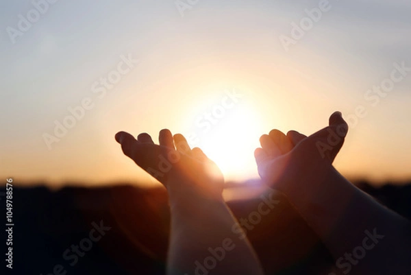 Obraz New Year's sunrise, brilliant light and rays of light shining through hands stretched out toward the rising sun, concept of hope and wishes for the future
