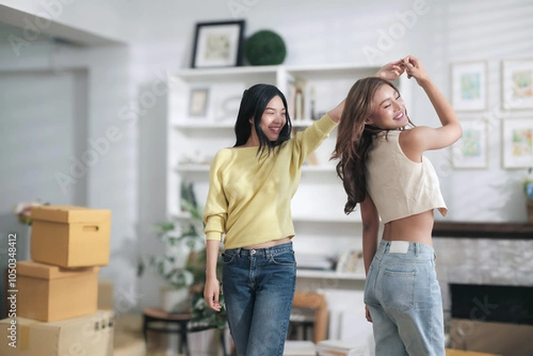 Fototapeta Two cute asian women are happily dancing in their home because they are delighted with their successful online business.
