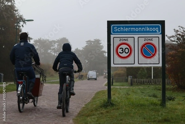 Obraz Two people are cycling near a place name sign (Schiermonnikoog in the Netherlands)