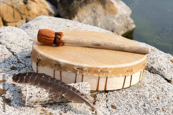 Fototapeta An image of a handmade leather meditation drum with white sage smudge stick and sacred feather.