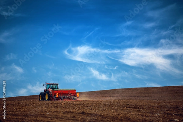 Fototapeta Farmer with tractor seeding crops at field
