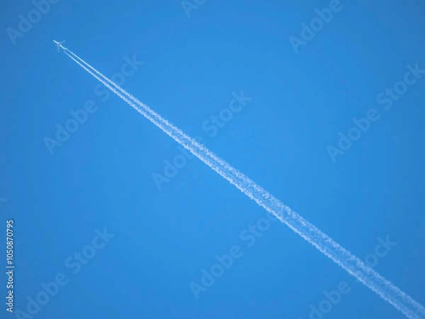 Fototapeta White streaks of planes leave behind like artificial clouds crossing the image diagonally across the photograph on a blue sky background