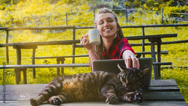 Fototapeta Freelancer woman enjoying coffee and petting cat while working o