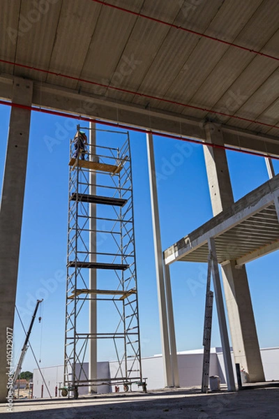 Obraz Painter is in action high up on scaffold with white color.