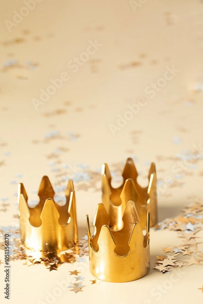Fototapeta Epiphany Day or Dia de Reyes Magos concept. Three gold crowns on beige background with star sparkling confetti