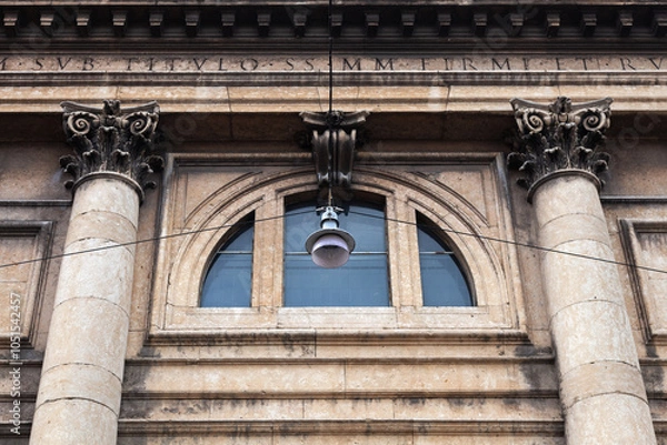 Fototapeta A street lamp hanging on wires against the backdrop of a building facade with columns and a large thermal window.