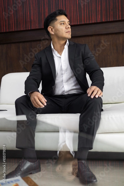 Fototapeta sitting on a sofa, a young man with short hair, black elegant suit and white shirt, portrait of a professional and lifestyle, people