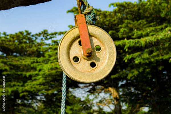Fototapeta Old wheel pulley with blue rope isolated on blurred outdoor background. Focus on. Noise. Exposure. Similar others