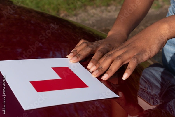 Obraz Hampshire England UK. 27.10.2024. Learner driver attaching L plate to bonnet of a red car.