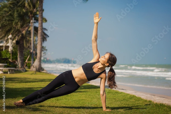 Obraz Молодая женщина занимается йогой на берегу моря. Боковая планка.