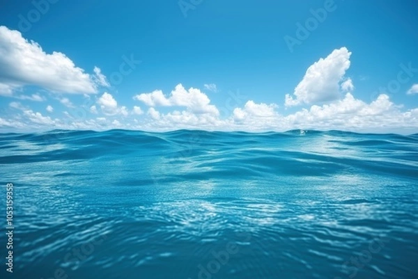 Fototapeta Open ocean view with gentle waves and clear blue sky scattered with fluffy white clouds, capturing the vastness and serenity of the sea