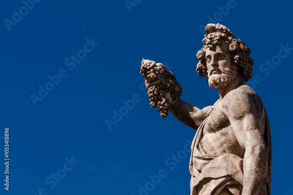 Fototapeta Paganism in Ancient Times. Roman or Greek god Bacchus holding grapes, a baroque statue, erected in the 17th century on Holy Trinity Bridge in Florence historic center (with blue sky and copy space)