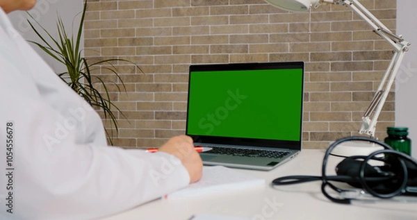 Fototapeta Medical worker studying online on green screen chroma key laptop. Doctor passing a training online using laptop.
