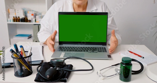Fototapeta Green screen laptop mockup doctor explaining in white gown while sitting in health clinic. Doctorate having online conference.