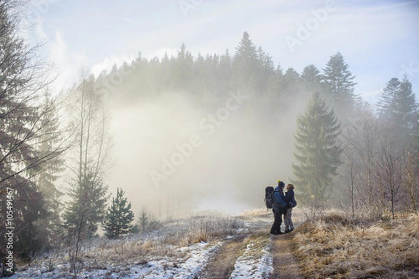 Fototapeta young couple of tourists staying in the winter woods on the road and look at each other, Carpathians Ukraine