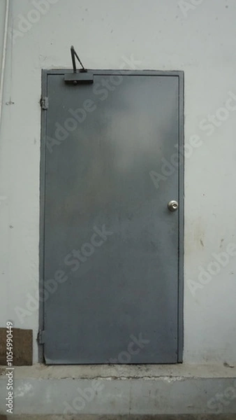 Fototapeta The door of a gray room at the back of a building
