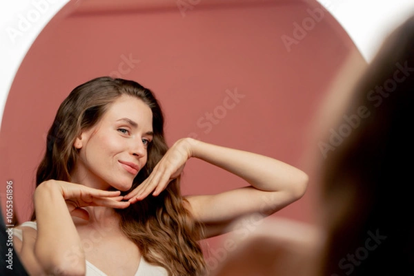 Fototapeta studio beauty shoot on pink background beautiful girl in white underwear admiring herself in the mirror smiling eyelashes beauty salon hands near her face