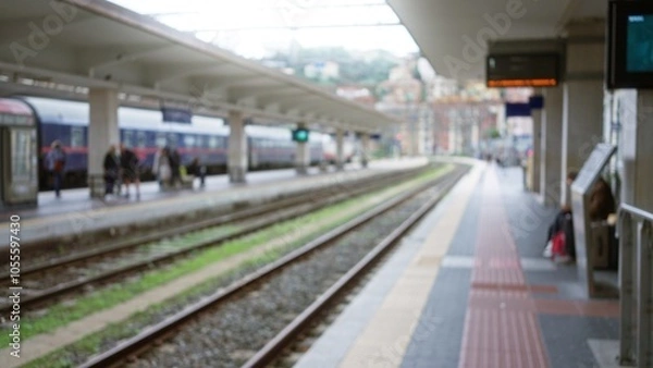 Fototapeta Blurred passengers stand at a railway station with defocused trains in the background, capturing a sense of motion and travel in the bustling urban setting.