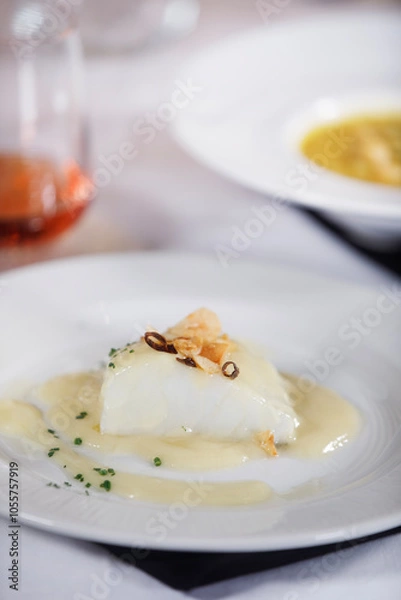 Fototapeta Dish of delicious cod fillet with a sauce and some garlic and pepper on top of it with rose wine at background.