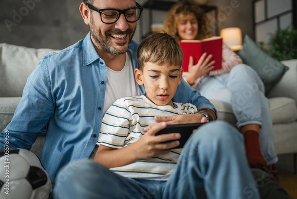 Fototapeta dad and son and play video games on cellphone with mum behind