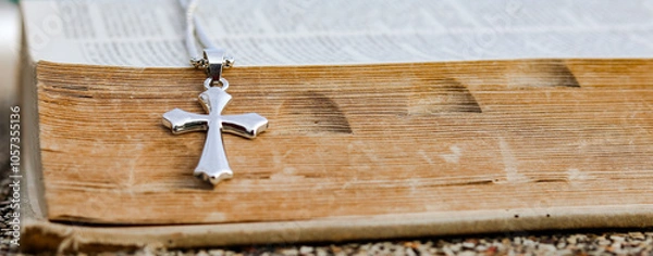 Fototapeta Shiny metal cross leaning against an old open book symbolizing the spread of Jesus Christs love among Christians reflecting faith devotion and the importance of Christian teachings.
