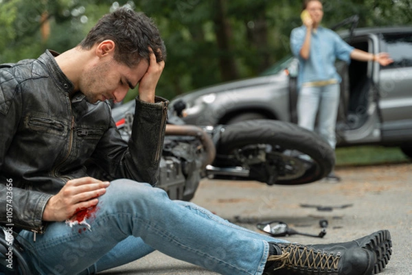 Obraz Motorcyclist sits on the asphalt near motorcycle, after road accidents with car. Broken and wrecked motorcycle on road