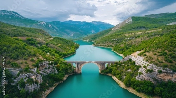 Fototapeta The lake water is blue-green, surrounded by green mountains and forests on both sides of the river, with an ancient stone arch bridge across it