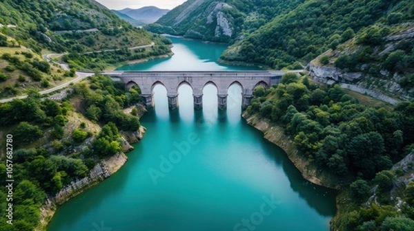 Fototapeta The lake water is blue-green, surrounded by green mountains and forests on both sides of the river, with an ancient stone arch bridge across it