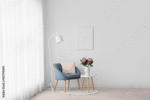 Fototapeta Armchair, lamp and coffee table with protea flowers in vase near white wall