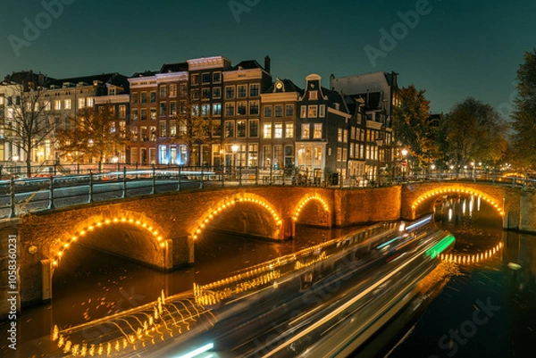 Obraz Amsterdam’s historic canal bridges illuminated at night. The Keizersgracht and Reguliersgracht intersection glows romantically, reflecting typical Dutch architecture and city lights in the water.