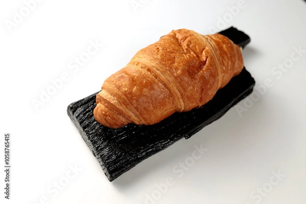 Fototapeta Crispy hot croissant on a black rectangular wooden board on a white background