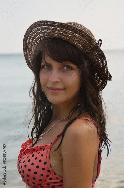 Obraz A young beautiful dark-skinned girl with blue eyes wearing a hat. Portrait of a woman in a swimsuit against the background of the sea.