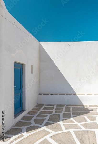 Obraz A striking example of traditional Cyclades architecture, this space showcases whitewashed walls and a blue door under bright sunlight, creating a serene atmosphere.