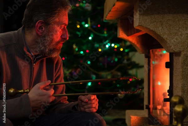 Obraz Man sits in front of burning fireplace. Behind Christmas tree